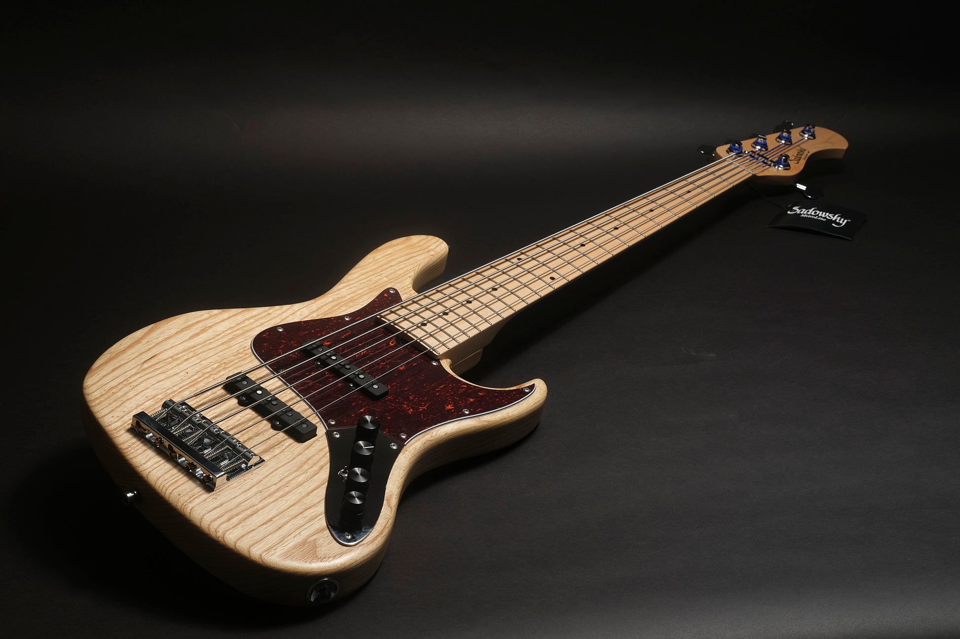 Electric bass guitar with a light wood finish on a black background