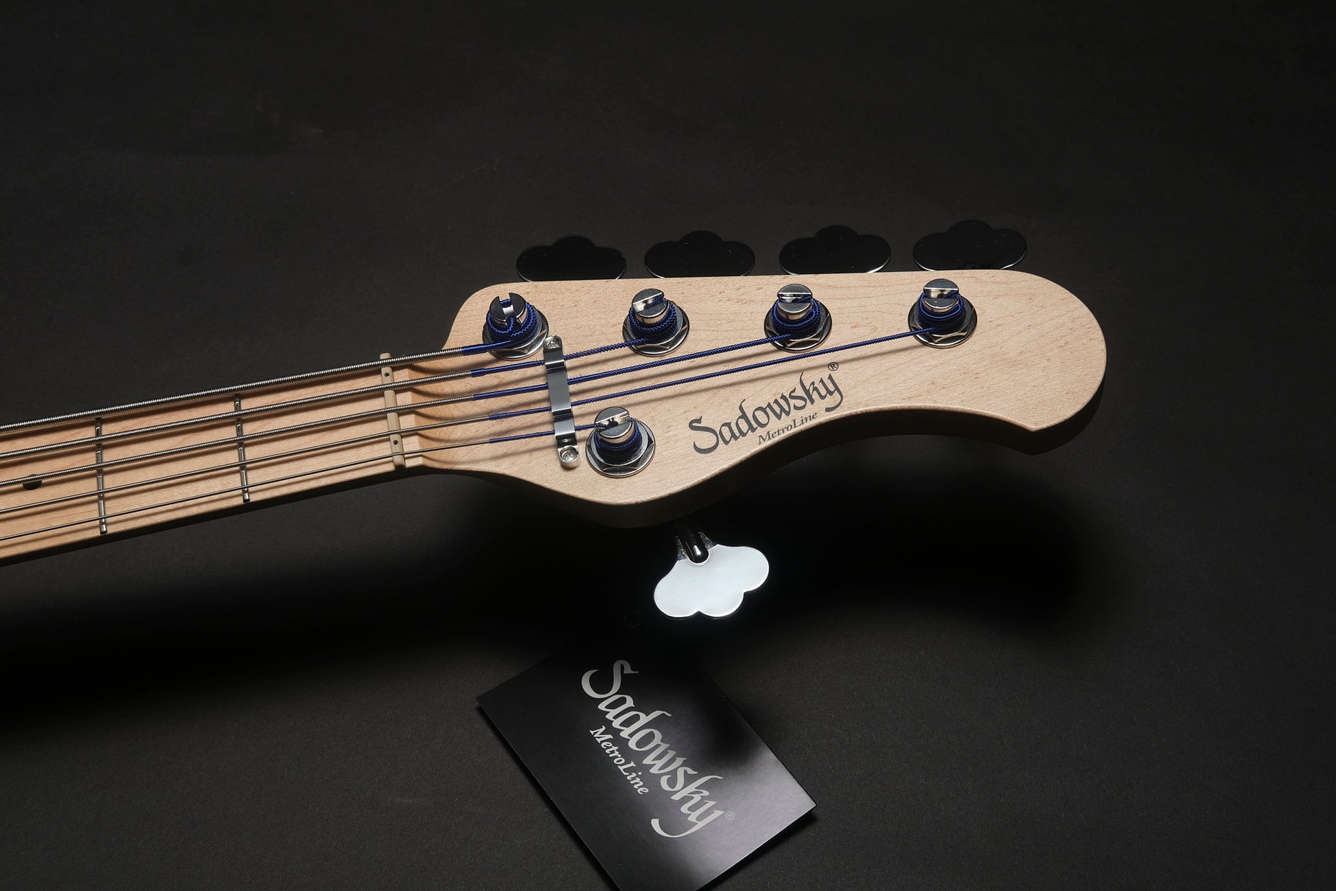 Sadowsky guitar neck with pick and branded card on a black background